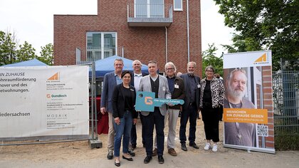 Nadine Otto übergibt für das Gundlach Bauunternehmen den Schlüssel mit dem Text 'Hier beginnt Zuhause'. Das Bauprojekt für Menschen in Wohnungsnot umfasst 7 Wohneinheiten. Schlüsselfertig gebaut.