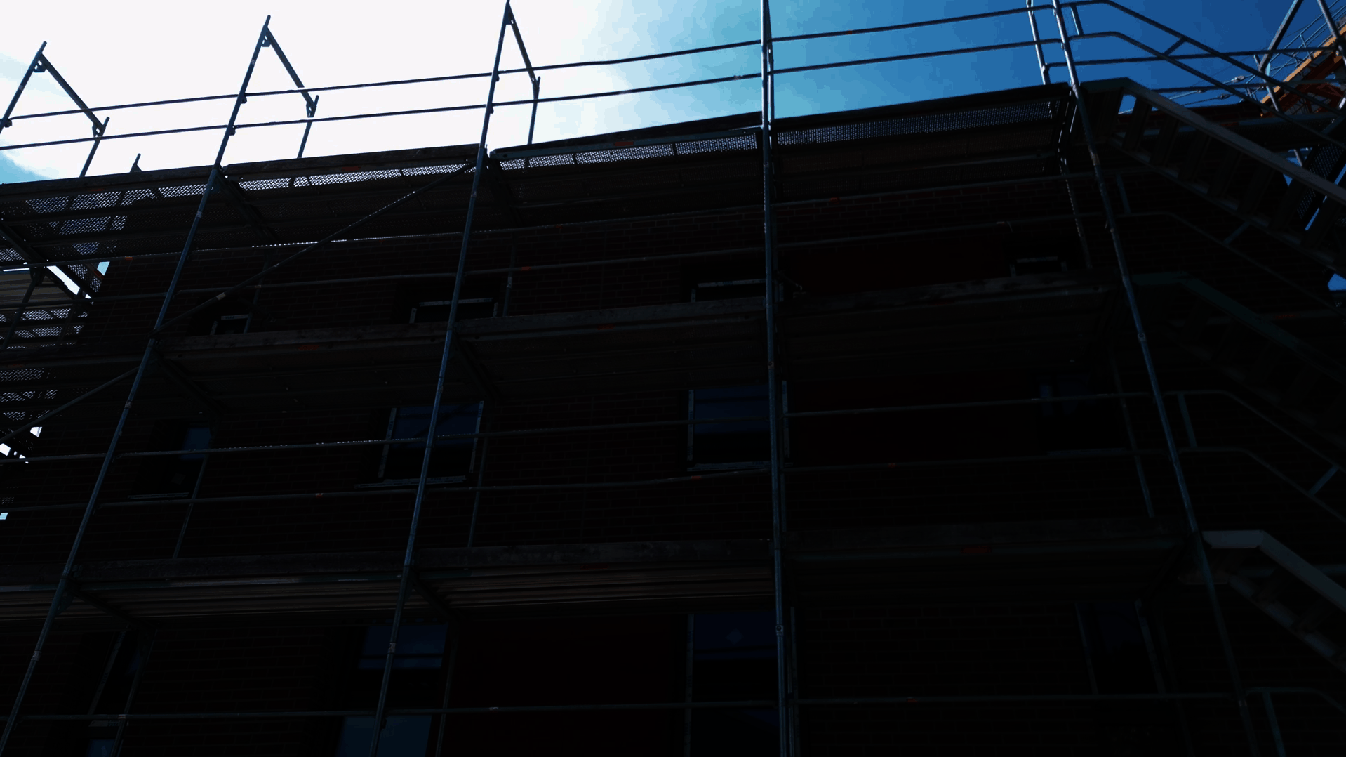 Ein mehrstöckiges Backsteingebäude mit Gerüsten an der Fassade steht im Vordergrund.