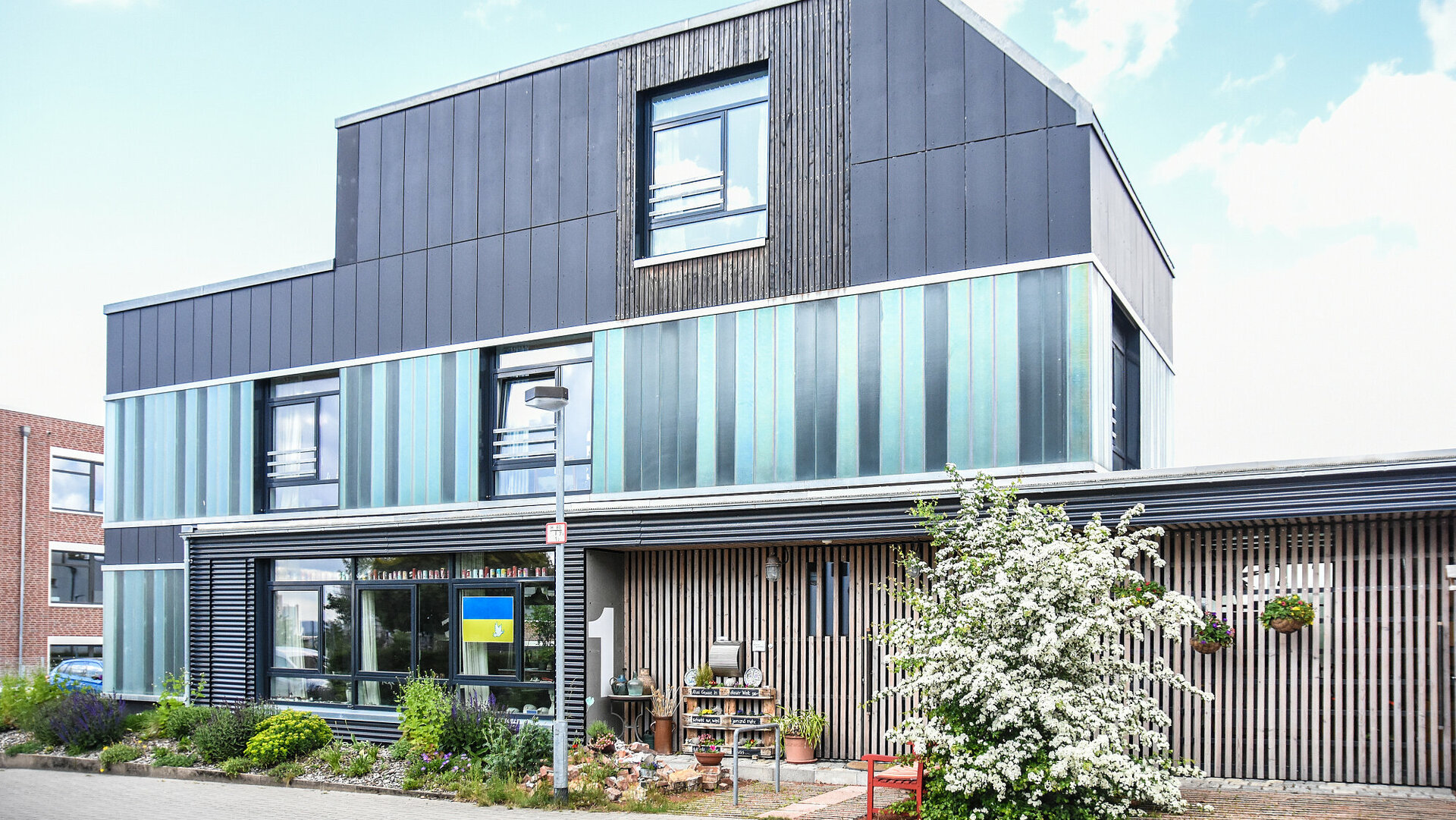 Das Recyclinghaus von vorne. Die grünlich-bläulichen Profilbaugläser waren einst an einer Lackiererei angebracht, die Faserzementplatten stammen aus einem Freizeitheim.