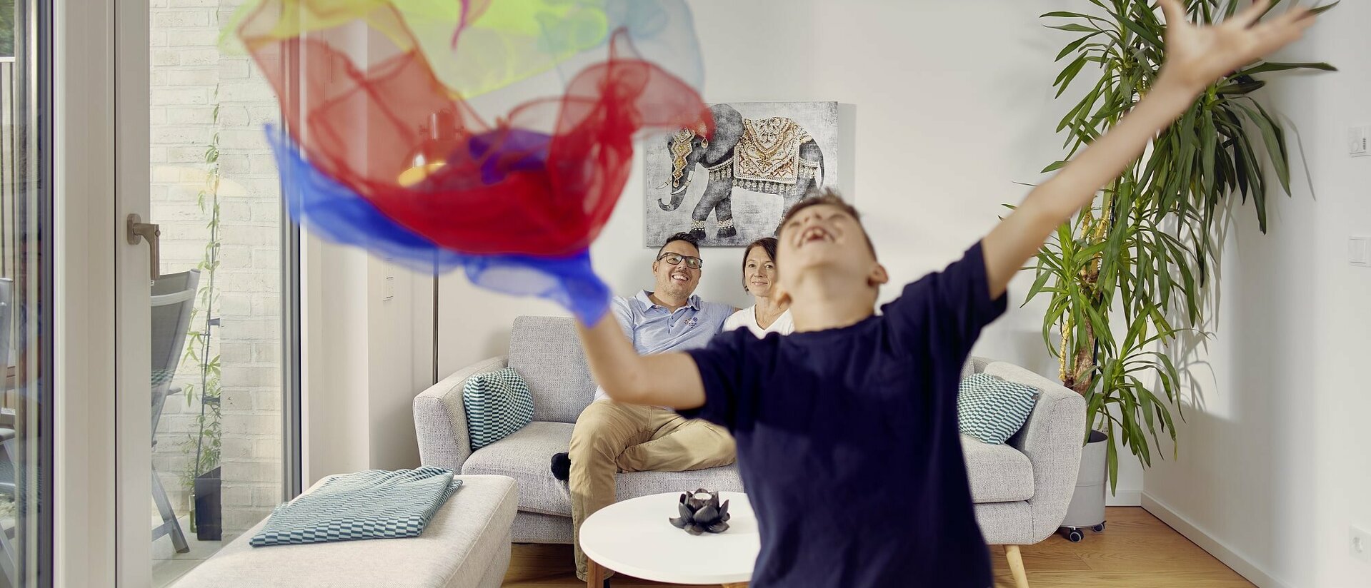 Familie im Reihenhaus Hannover. Junge wirft bunte Tücher in die Luft und freut sich.