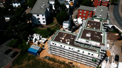 Luftaufnahme eines modernen Gebäudekomplexes mit zwei rechteckigen Flachdachbauten, die sich im Bau befinden. Die Fassaden sind eingerüstet, Baumaterialien und Baucontainer stehen auf dem Gelände. Im Kontext handelt es sich um Micro Apartments für ehemals wohnungslose Menschen in der Büttnerstraße, die durch das Generalunternehmen Gundlach erbaut wurden.