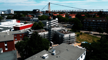 Luftaufnahme eines modernen Gebäudekomplexes mit zwei rechteckigen Flachdachbauten, die sich im Bau befinden. Die Fassaden sind eingerüstet, Baumaterialien und Baucontainer stehen auf dem Gelände. Im Kontext handelt es sich um Micro Apartments für ehemals wohnungslose Menschen in der Büttnerstraße, die durch das Generalunternehmen Gundlach erbaut wurden.