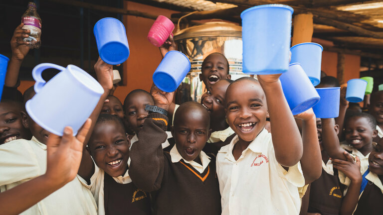 Kinder in Ugandas Hauptstadt Kampala halten Trinkbecher in die Höhe.