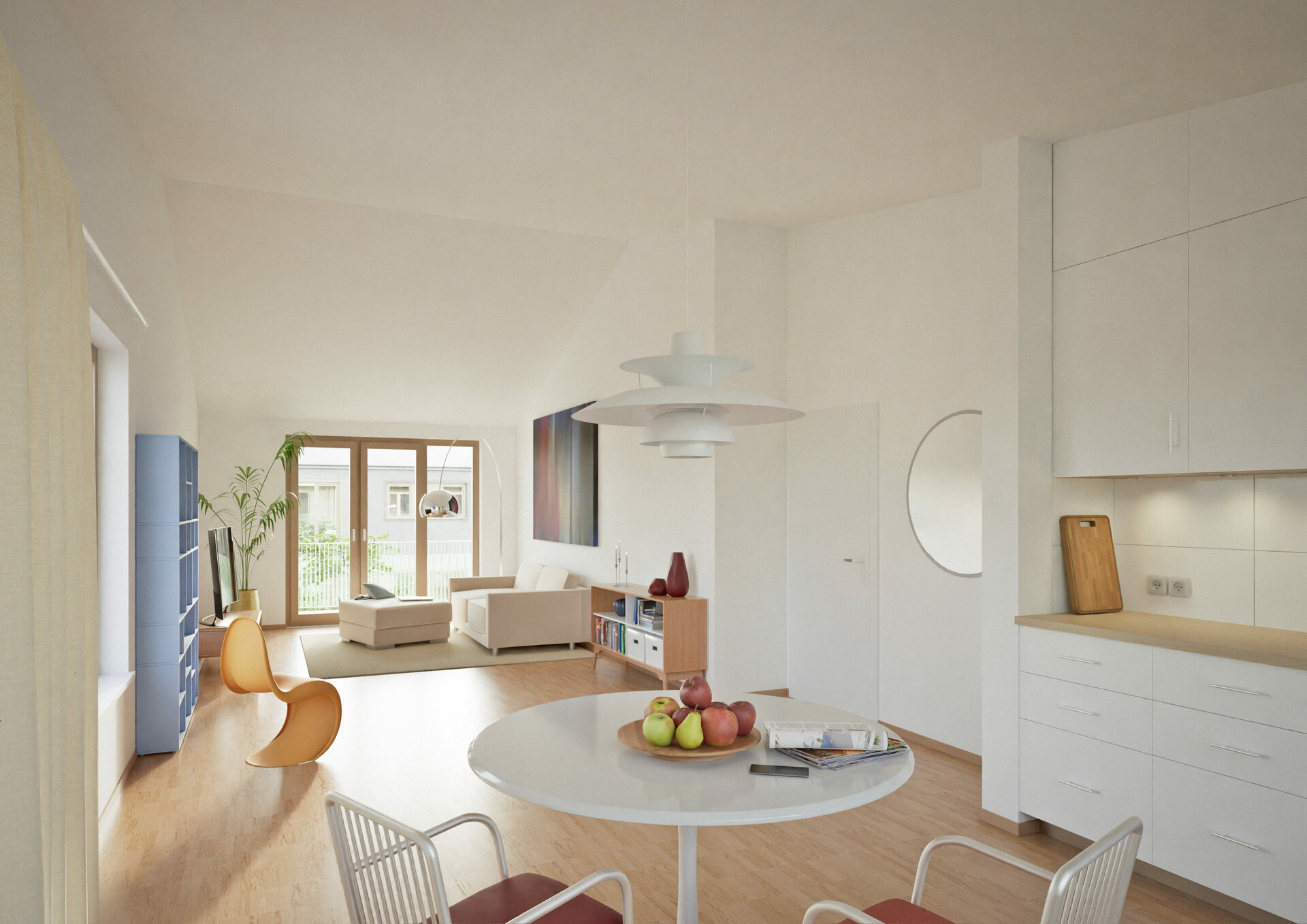 Helles Wohnzimmer in der Dachgeschosswohnung des Wohnprojekts »Aufwind – Heute wohnen. An morgen denken.«. Im Vordergrund steht ein runder Esstisch mit vier weißen Stühlen, darauf eine Obstschale und eine Zeitschrift. Die offene Küche ist rechts mit weißen Schränken und einer Arbeitsplatte ausgestattet. Im Hintergrund befindet sich ein Wohnbereich mit einem hellen Sofa, einem niedrigen Couchtisch und einem TV auf einem blauen Sideboard. Zwei orangefarbene Stühle stehen am Fenster, das viel Tageslicht hereinlässt. Der Raum ist mit Holzfußboden ausgelegt und wirkt freundlich und modern.