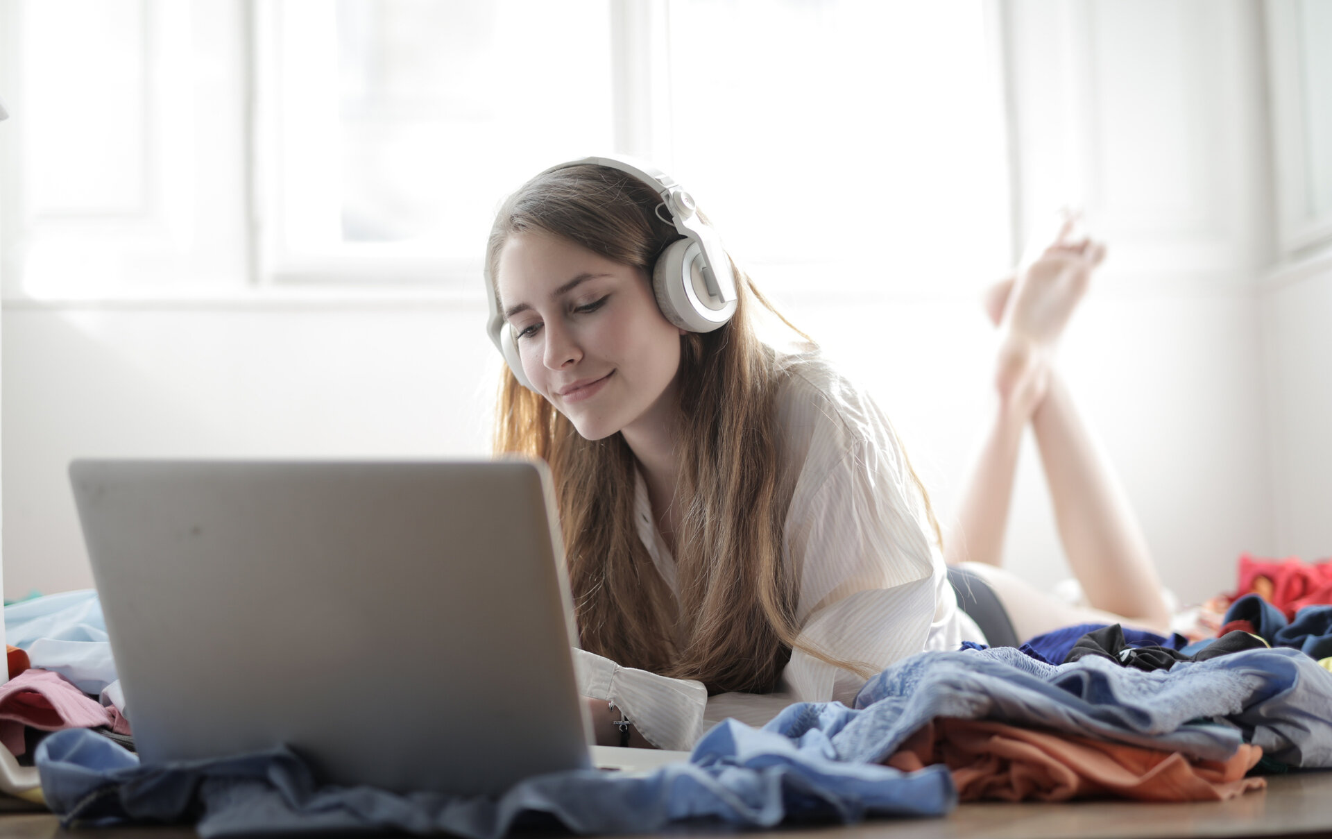 Frau im weißen Shirt, auf dem Sofa, trägt Kopfhörer und bedient MacBook.