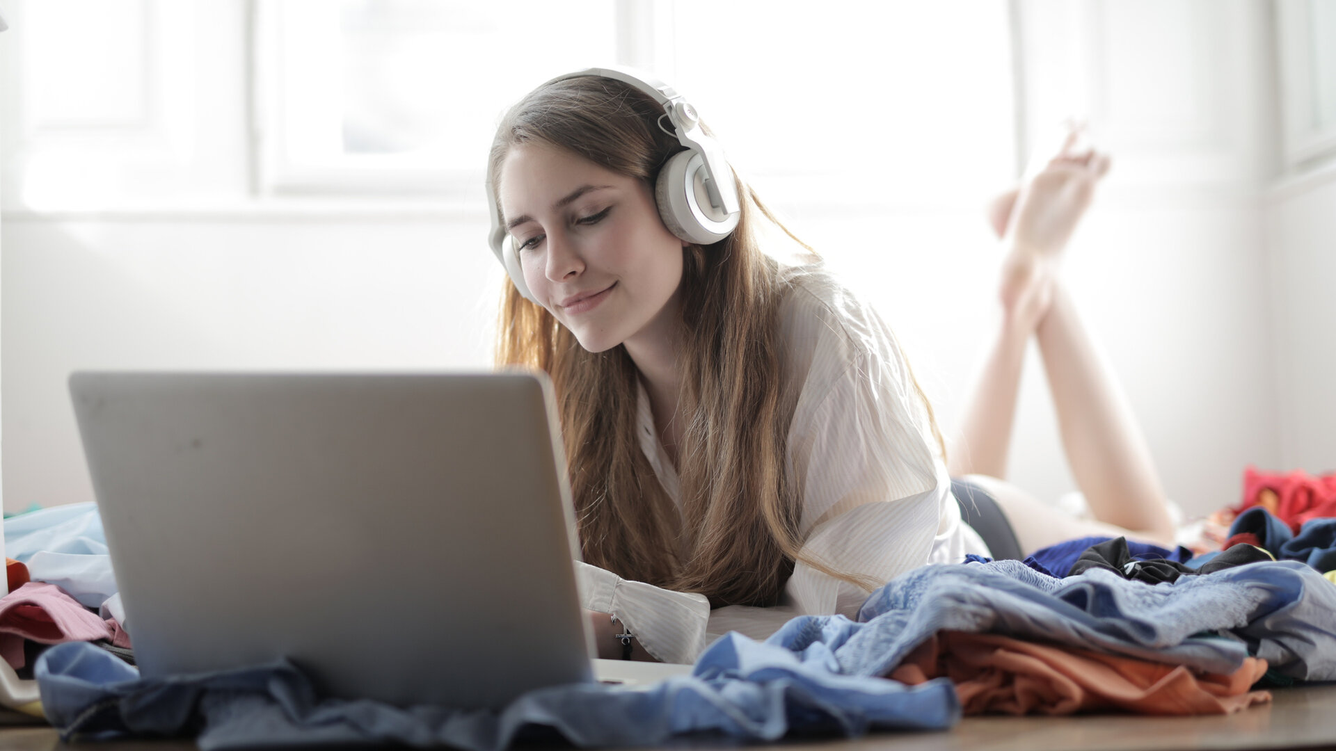 Frau im weißen Shirt, auf dem Sofa, trägt Kopfhörer und bedient MacBook.
